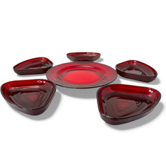 Vintage Anchor Hocking Royal Ruby relish trays arranged in a circular pattern around a coordinating red glass plate. The translucent ruby red glass glows with depth and symmetry, showcasing the sculptural triangular shapes and rich mid-century color. Ideal for holiday styling or vintage table settings.