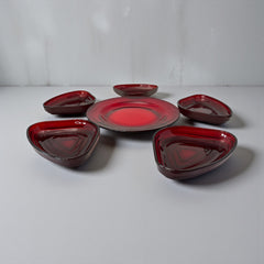 Vintage Anchor Hocking Royal Ruby relish trays arranged in a circular pattern around a coordinating red glass plate. The translucent ruby red glass glows with depth and symmetry, showcasing the sculptural triangular shapes and rich mid-century color. Ideal for holiday styling or vintage table settings.