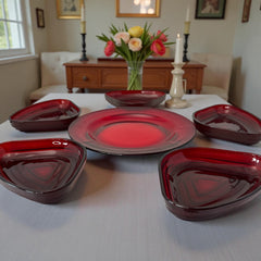 Vintage Anchor Hocking Royal Ruby relish trays arranged in a circular pattern around a coordinating red glass plate. The translucent ruby red glass glows with depth and symmetry, showcasing the sculptural triangular shapes and rich mid-century color. Ideal for holiday styling or vintage table settings.