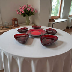 Vintage Anchor Hocking Royal Ruby relish trays arranged in a circular pattern around a coordinating red glass plate. The translucent ruby red glass glows with depth and symmetry, showcasing the sculptural triangular shapes and rich mid-century color. Ideal for holiday styling or vintage table settings.