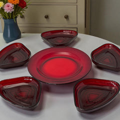 Vintage Anchor Hocking Royal Ruby relish trays arranged in a circular pattern around a coordinating red glass plate. The translucent ruby red glass glows with depth and symmetry, showcasing the sculptural triangular shapes and rich mid-century color. Ideal for holiday styling or vintage table settings.