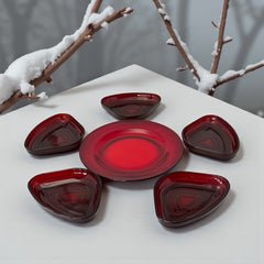 Vintage Anchor Hocking Royal Ruby relish trays arranged in a circular pattern around a coordinating red glass plate. The translucent ruby red glass glows with depth and symmetry, showcasing the sculptural triangular shapes and rich mid-century color. Ideal for holiday styling or vintage table settings.
