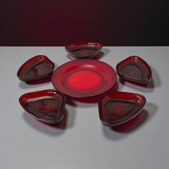 Vintage Anchor Hocking Royal Ruby relish trays arranged in a circular pattern around a coordinating red glass plate. The translucent ruby red glass glows with depth and symmetry, showcasing the sculptural triangular shapes and rich mid-century color. Ideal for holiday styling or vintage table settings.