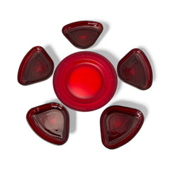 Vintage Anchor Hocking Royal Ruby relish trays arranged in a circular pattern around a coordinating red glass plate. The translucent ruby red glass glows with depth and symmetry, showcasing the sculptural triangular shapes and rich mid-century color. Ideal for holiday styling or vintage table settings.
