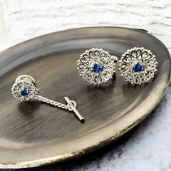 Vintage Anson men’s jewelry set featuring silver-tone round cufflinks and matching tie tack with blue rhinestones and openwork filigree design; presented in original moss green velvet-lined box, all pieces signed and in excellent condition.