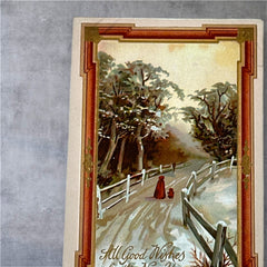 Antique 1910s embossed postcard featuring a snowy path with a person and child walking, framed by gilded orange-brown border; message reads “All Good Wishes for the New Year.