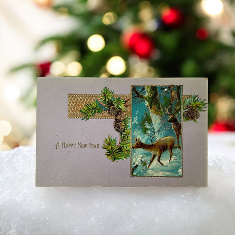 Antique 1912 New Year postcard featuring embossed deer in snowy forest with pinecones and gold gilt, muted lavender background, greeting “A Happy New Year” in capital letters, very good condition with minimal corner wear.
