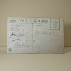 Antique 1912 New Year postcard featuring embossed deer in snowy forest with pinecones and gold gilt, muted lavender background, greeting “A Happy New Year” in capital letters, very good condition with minimal corner wear.