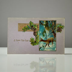 Antique 1912 New Year postcard featuring embossed deer in snowy forest with pinecones and gold gilt, muted lavender background, greeting “A Happy New Year” in capital letters, very good condition with minimal corner wear.