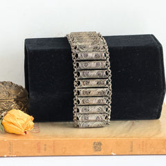 Antique Balkan cannetille silver bracelet with ornate filigree links, side chains, and a long pin clasp, shown in its natural patina.