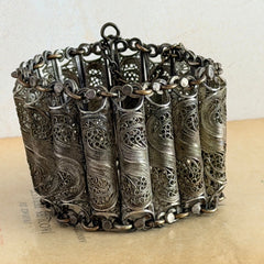 Antique Balkan cannetille silver bracelet with ornate filigree links, side chains, and a long pin clasp, shown in its natural patina.