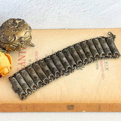 Antique Balkan cannetille silver bracelet with ornate filigree links, side chains, and a long pin clasp, shown in its natural patina.