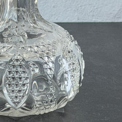 Antique pressed clear glass cruet with diamond pattern and rounded base.