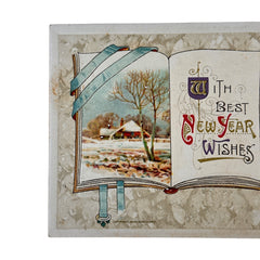 Antique embossed German New Year postcard from the 1910s featuring an open book with snowy countryside illustration, festive holly sprig, and ornate greeting text.