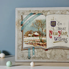 Antique embossed German New Year postcard from the 1910s featuring an open book with snowy countryside illustration, festive holly sprig, and ornate greeting text.