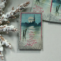 Antique 1910s New Year postcard showing a silver moonlit church and town skyline reflected on a river, with ornate red lettering “To Wish You A Happy New Year” and handwritten family message on reverse, very good condition with light corner wear.