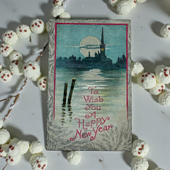 Antique 1910s New Year postcard showing a silver moonlit church and town skyline reflected on a river, with ornate red lettering “To Wish You A Happy New Year” and handwritten family message on reverse, very good condition with light corner wear.