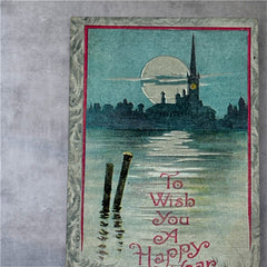 Antique 1910s New Year postcard showing a silver moonlit church and town skyline reflected on a river, with ornate red lettering “To Wish You A Happy New Year” and handwritten family message on reverse, very good condition with light corner wear.