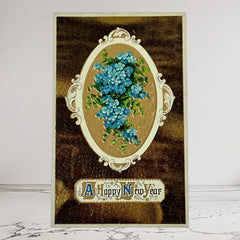 Antique 1910s New Year postcard featuring embossed blue forget-me-not flowers in a gold-gilded oval frame, set against a textured brown background resembling crocodile skin; elegant and well-preserved with handwritten 1913 message on reverse.