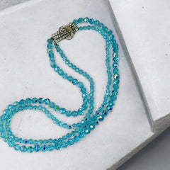 Vintage double‑strand aqua blue AB crystal necklace with faceted beads and a silver‑tone pavé rhinestone brooch clasp, shown from multiple angles to highlight bead size, sparkle, and clasp detailing.