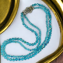 Vintage double‑strand aqua blue AB crystal necklace with faceted beads and a silver‑tone pavé rhinestone brooch clasp, shown from multiple angles to highlight bead size, sparkle, and clasp detailing.