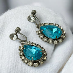 A pair of vintage 1950s–60s silver‑tone screw‑back earrings with aqua pear rhinestones and clear accent stones, shown from different angles to highlight their shape and condition.