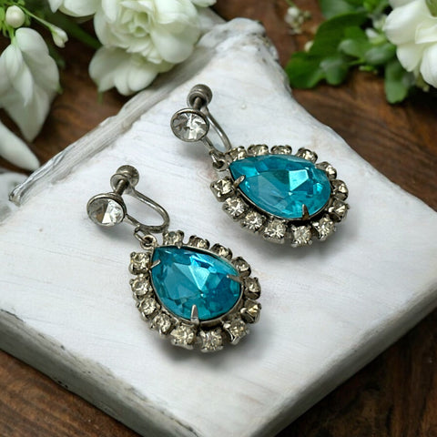 A pair of vintage 1950s–60s silver‑tone screw‑back earrings with aqua pear rhinestones and clear accent stones, shown from different angles to highlight their shape and condition.