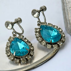 A pair of vintage 1950s–60s silver‑tone screw‑back earrings with aqua pear rhinestones and clear accent stones, shown from different angles to highlight their shape and condition.