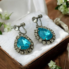 A pair of vintage 1950s–60s silver‑tone screw‑back earrings with aqua pear rhinestones and clear accent stones, shown from different angles to highlight their shape and condition.