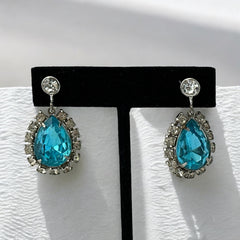 A pair of vintage 1950s–60s silver‑tone screw‑back earrings with aqua pear rhinestones and clear accent stones, shown from different angles to highlight their shape and condition.