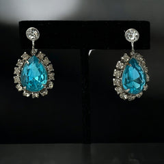 A pair of vintage 1950s–60s silver‑tone screw‑back earrings with aqua pear rhinestones and clear accent stones, shown from different angles to highlight their shape and condition.