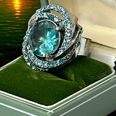 Adjustable silver-tone cocktail ring with a large round aqua rhinestone cabochon and open swirl design set with smaller teal rhinestones; vintage-inspired statement jewelry in very good condition.