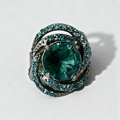 Adjustable silver-tone cocktail ring with a large round aqua rhinestone cabochon and open swirl design set with smaller teal rhinestones; vintage-inspired statement jewelry in very good condition.