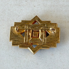 Vintage Art Deco style gold‑tone brooch with black enamel and clear rhinestones, geometric design photographed on antique French script background.