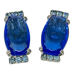 Vintage clip-on earrings featuring large cobalt blue oval rhinestones with light blue chaton accents in silver-tone Art Deco-style settings, mid-century design.