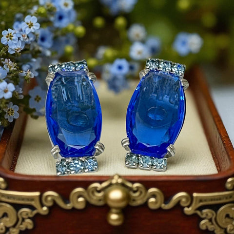 Vintage clip-on earrings featuring large cobalt blue oval rhinestones with light blue chaton accents in silver-tone Art Deco-style settings, mid-century design.