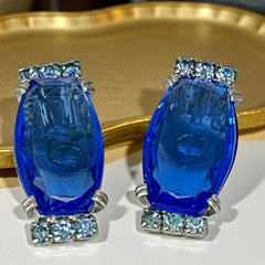 Vintage clip-on earrings featuring large cobalt blue oval rhinestones with light blue chaton accents in silver-tone Art Deco-style settings, mid-century design.