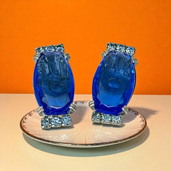 Vintage clip-on earrings featuring large cobalt blue oval rhinestones with light blue chaton accents in silver-tone Art Deco-style settings, mid-century design.