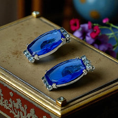 Vintage clip-on earrings featuring large cobalt blue oval rhinestones with light blue chaton accents in silver-tone Art Deco-style settings, mid-century design.