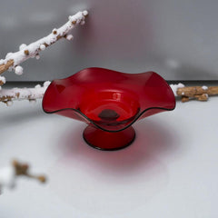 Vintage ruby red hand-blown glass bowl with a freeform wavy rim and clear pedestal base, photographed from above to highlight its organic curves and glossy surface. Midcentury compote style, ideal for decorative or serving use.