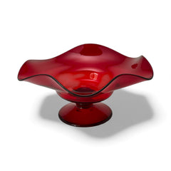 Vintage ruby red hand-blown glass bowl with a freeform wavy rim and clear pedestal base, photographed from above to highlight its organic curves and glossy surface. Midcentury compote style, ideal for decorative or serving use.