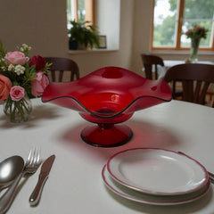 Vintage ruby red hand-blown glass bowl with a freeform wavy rim and clear pedestal base, photographed from above to highlight its organic curves and glossy surface. Midcentury compote style, ideal for decorative or serving use.