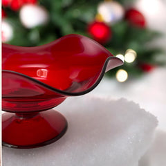 Vintage ruby red hand-blown glass bowl with a freeform wavy rim and clear pedestal base, photographed from above to highlight its organic curves and glossy surface. Midcentury compote style, ideal for decorative or serving use.