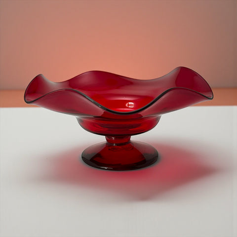 Vintage ruby red hand-blown glass bowl with a freeform wavy rim and clear pedestal base, photographed from above to highlight its organic curves and glossy surface. Midcentury compote style, ideal for decorative or serving use.