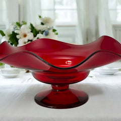 Vintage ruby red hand-blown glass bowl with a freeform wavy rim and clear pedestal base, photographed from above to highlight its organic curves and glossy surface. Midcentury compote style, ideal for decorative or serving use.