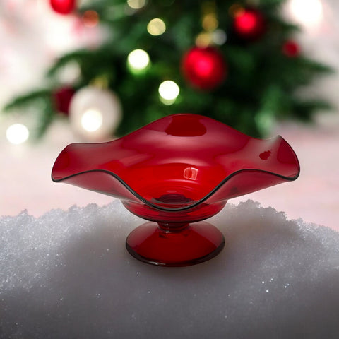 Vintage ruby red hand-blown glass bowl with a freeform wavy rim and clear pedestal base, photographed from above to highlight its organic curves and glossy surface. Midcentury compote style, ideal for decorative or serving use.