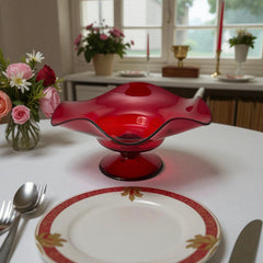 Vintage ruby red hand-blown glass bowl with a freeform wavy rim and clear pedestal base, photographed from above to highlight its organic curves and glossy surface. Midcentury compote style, ideal for decorative or serving use.