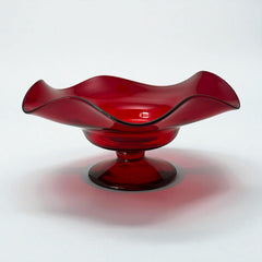 Vintage ruby red hand-blown glass bowl with a freeform wavy rim and clear pedestal base, photographed from above to highlight its organic curves and glossy surface. Midcentury compote style, ideal for decorative or serving use.