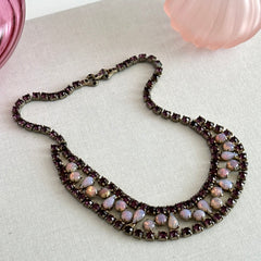 A vintage Astra necklace featuring glowing faux opal cabochons and deep amethyst stones in a double‑row midcentury design, shown on a neutral background to highlight its color and detail.