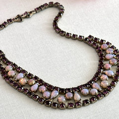 A vintage Astra necklace featuring glowing faux opal cabochons and deep amethyst stones in a double‑row midcentury design, shown on a neutral background to highlight its color and detail.